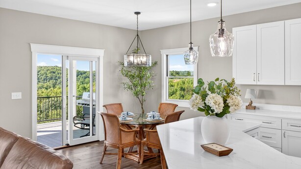 Una cocina moderna con armarios blancos, un comedor con sillas de mimbre, una mesa de vidrio y vistas a la vegetación a través de puertas correderas de cristal.
