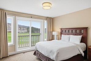 Una camera d'albergo con un letto grande, un comodino, una lampada e vista su un campo da golf attraverso una porta scorrevole in vetro.
