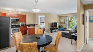 Een moderne keuken met roestvrijstalen apparatuur, een eethoek met rieten stoelen, een woonkamer met televisie en zitplaatsen, en een balkon met uitzicht.