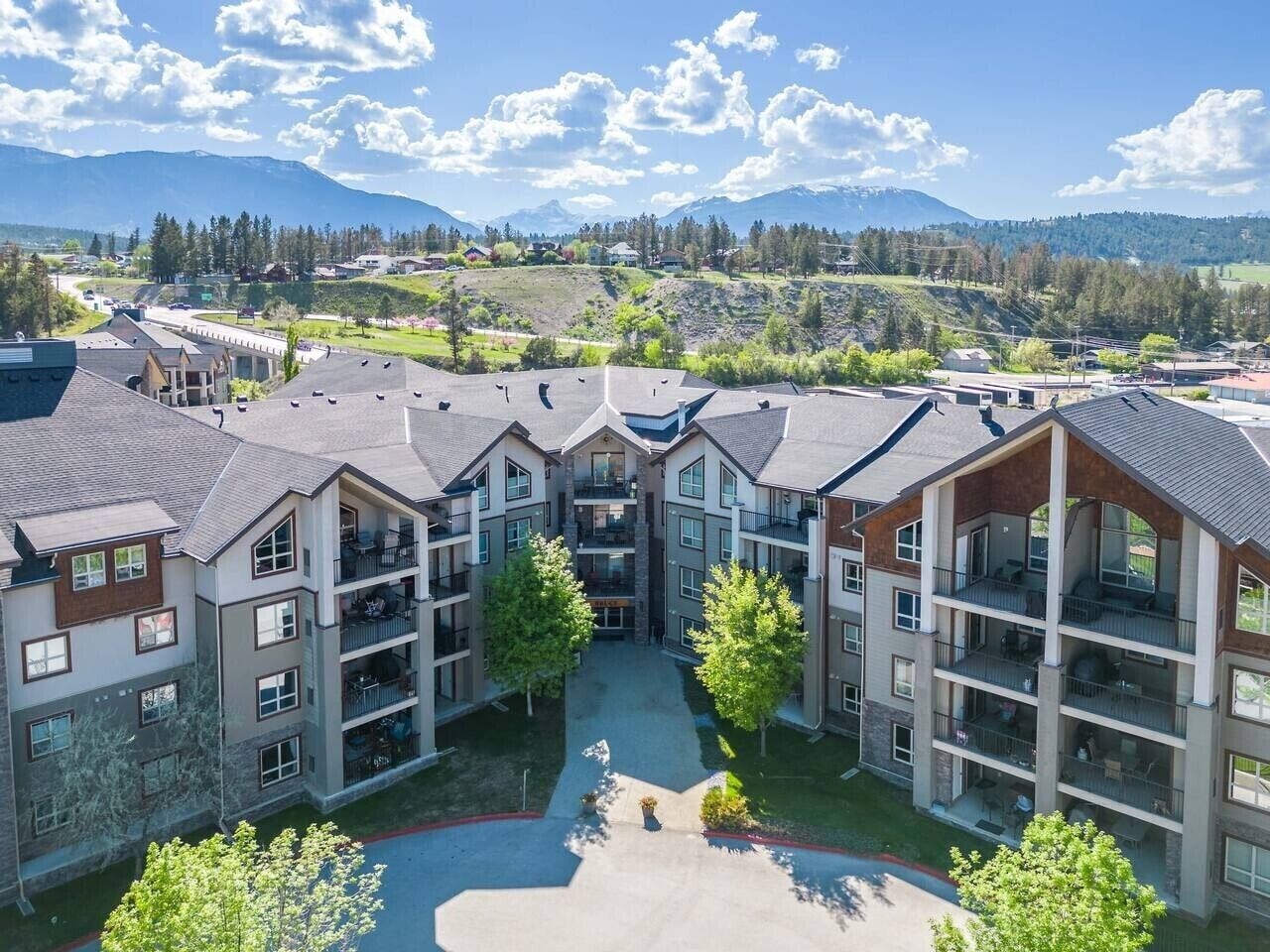 Un immeuble résidentiel à plusieurs étages, doté de balcons, d’une cour intérieure et surplombant un paysage montagneux.