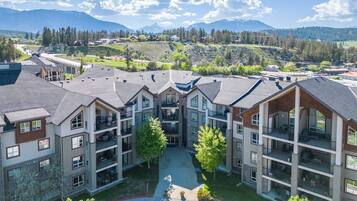 Un immeuble résidentiel à plusieurs étages, doté de balcons, d’une cour intérieure et surplombant un paysage montagneux.