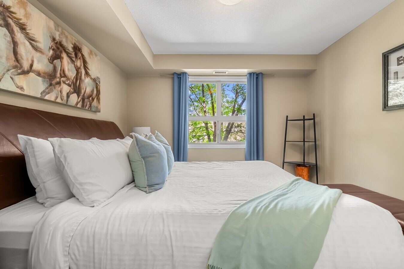 Une chambre à coucher avec un grand lit, une tête de lit, une fenêtre avec des rideaux et un tableau au mur.
