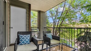 Een overdekt balkon met rieten stoelen en een barbecue.