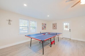A room with a ping pong table, a ceiling fan, and a door with a window.