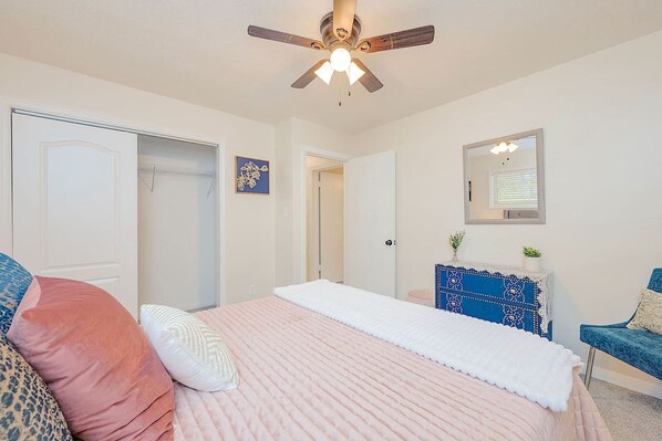 A bedroom with a bed, a ceiling fan, a dresser, and a chair.