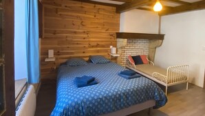 Una habitación con cama, una mesita, una silla, un calefactor y una ventana con cortinas.