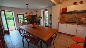 Un comedor con una mesa de madera, sillas, una planta en maceta y una cocina con armarios y una encimera.