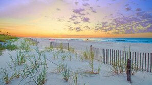 Una spiaggia con una recinzione di legno, dune di sabbia e un tramonto.