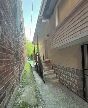 Ein schmaler Gang mit einer Backsteinmauer und einer Holztreppe, die zu einem Balkon führt.
