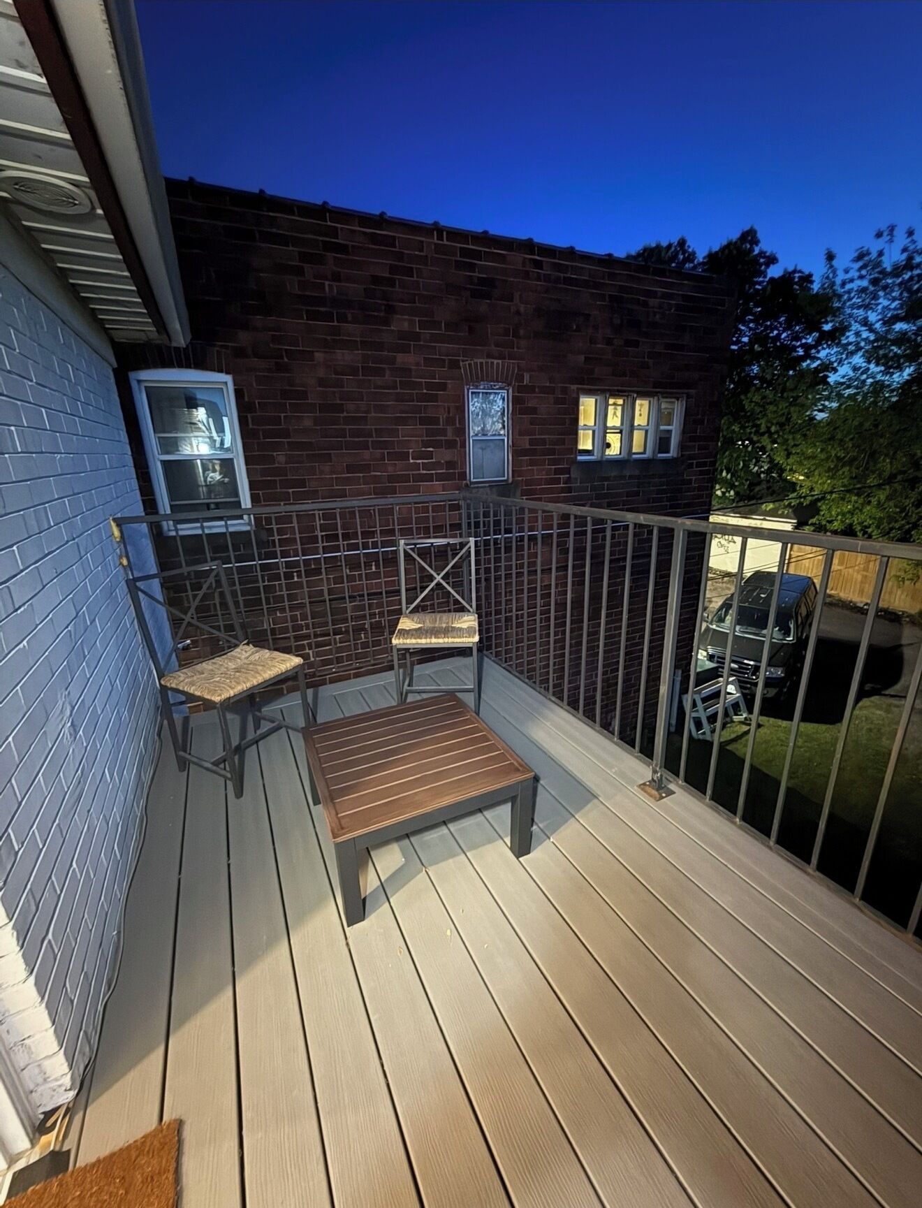 A wooden deck with a metal railing, a bench, and two chairs.