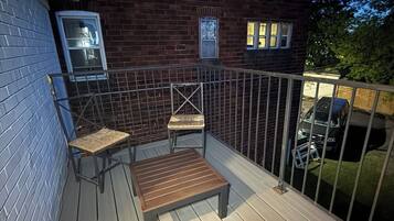 A wooden deck with a metal railing, a bench, and two chairs.
