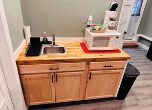 A kitchen with a wooden countertop, a microwave, a sink, and cabinets.