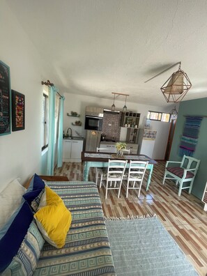A cozy living room with a sofa, a dining table with chairs, a kitchen area with cabinets and a stove, and a hanging light fixture. - Rancho Elquino (Vicuña)