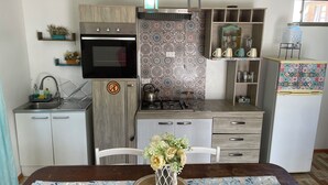 Cocina compacta con microondas, estufa y lavabo, una mesa de comedor con un florero, y azulejos con diseño.