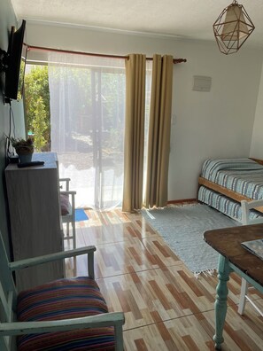 A room with a wooden floor, a bed with patterned bedding, a table with a notebook, a chair with a striped cushion, and a television on a stand. - Rancho Elquino (Vicuña)