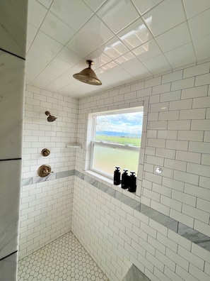Une salle de bain aux murs recouverts de carreaux de cĂ©ramique blancs, une fenĂȘtre offrant une vue agrĂ©able et trois bouteilles noires posĂ©es sur le rebord de la fenĂȘtre.