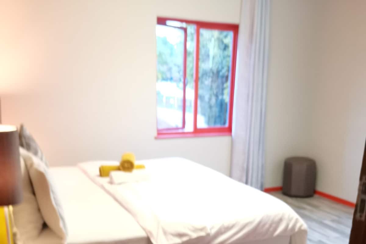 Un dormitorio con cama, mesita de noche, lámpara, ventana y felpudo.