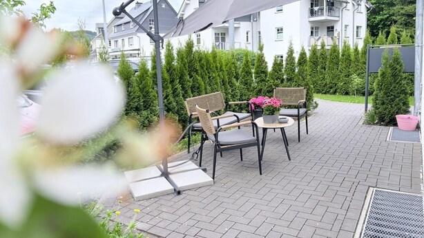 Un patio al aire libre con una mesa y sillas, un toldo gris y setos bien cuidados.