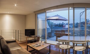 Ein modernes Wohnzimmer mit Flachbildfernseher, Couchtisch mit Büchern, Sofa und Essbereich mit Stühlen und Tisch.