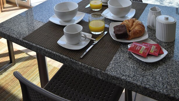 A breakfast table with a croissant, coffee cups, and juice, set on a balcony with a city view. - Beautiful superior duplex apartment (Santiago)