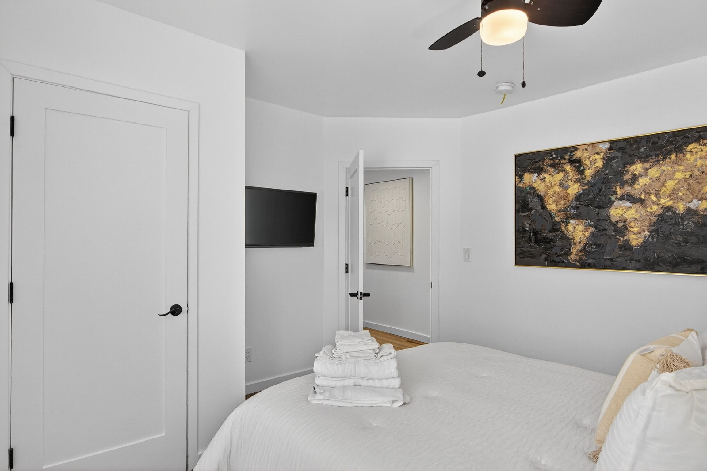 Ein Schlafzimmer mit einem Bett, einem Stapel gefalteter Handtücher, einem Deckenventilator, einer Tür und einem Bild an der Wand.