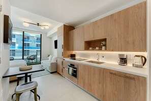A modern kitchen with wooden cabinets, a built-in oven, a coffee maker, and a large window overlooking a cityscape. - Crosby Miami WTC Studio Retreat #408 (Miami)