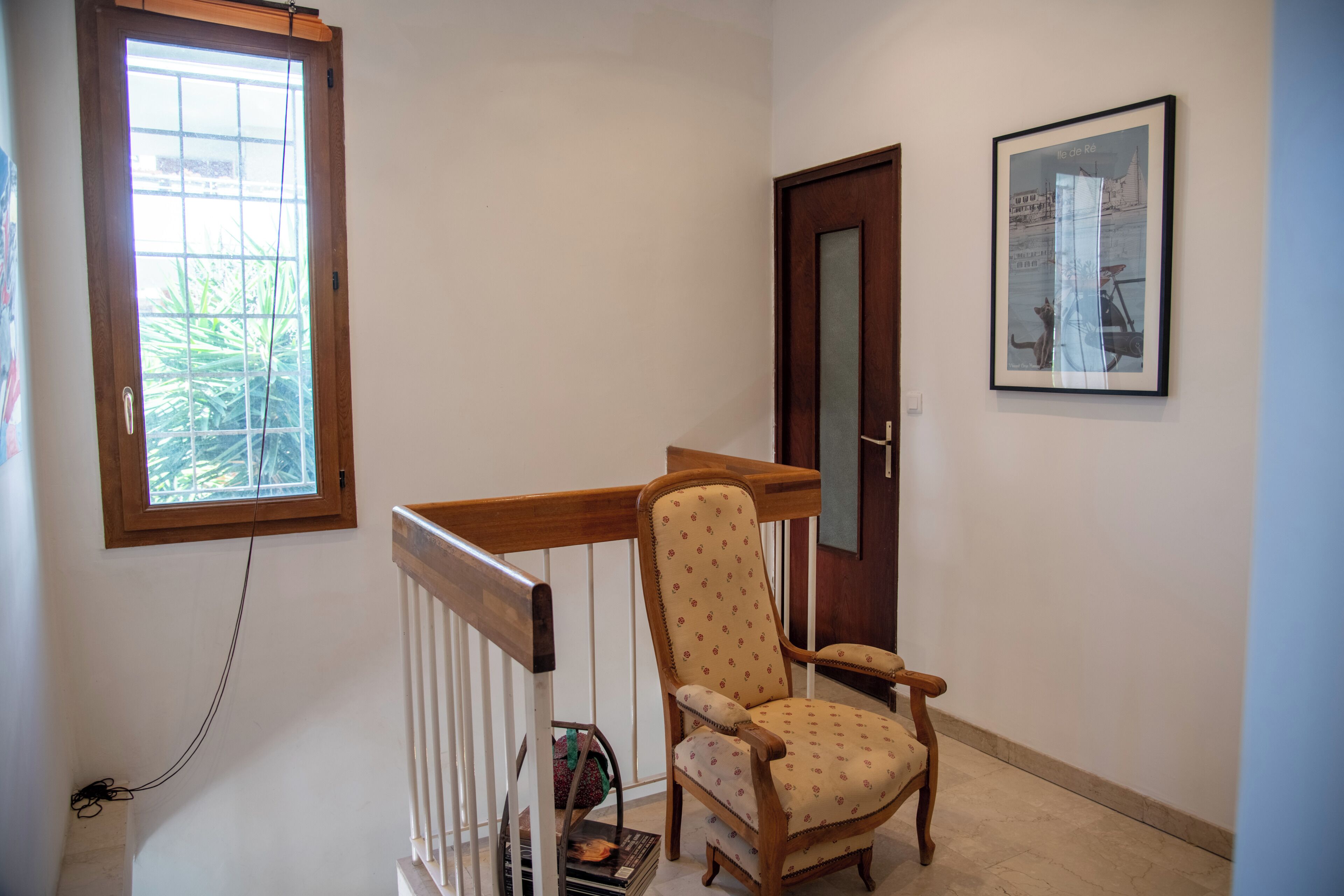 A room with a wooden chair, a door, a window, and a framed picture on the wall.