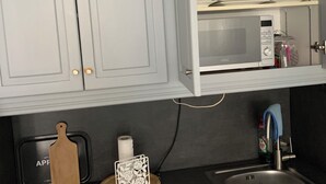 Een keuken met witte kastjes, een magnetron, een spoelbak en een aanrecht met een snijplank en een decoratief object.