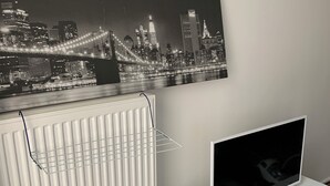 Een moderne woonkamer met een witte radiator, een witte tv-meubel, een flatscreen-tv, een afstandsbediening en een zwart-wit stadsgezicht schilderij aan de muur.
