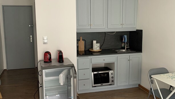 Een compacte keuken met grijze kastjes, een inbouwoven, een magnetron en een kleine eethoek met een tafel en stoelen.