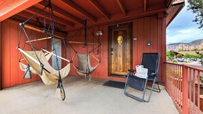 A porch with two hammocks, a folding chair, and a door with a wooden panel.