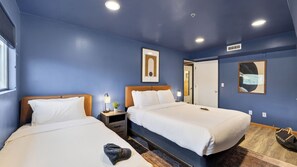Camera d'albergo con due letti, un comodino, una lampada, un quadro incorniciato e una porta.