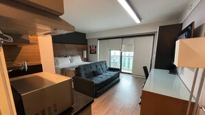 Una habitación de hotel moderna con kitchenette, sofá, cama y un ventanal grande.
