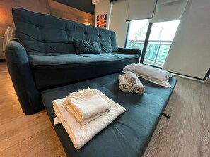 A modern living room with a dark blue sofa, a small table with rolled towels, and a flag on the wall. - FLAT HOTEL IBIRAPUERA  (São Paulo)