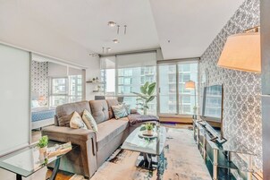 Un salon moderne avec un canapé gris, une table basse en verre et un papier peint à motifs.