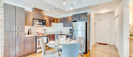A modern kitchen with stainless steel appliances, wooden cabinets, and a dining area with a glass table and chairs.
