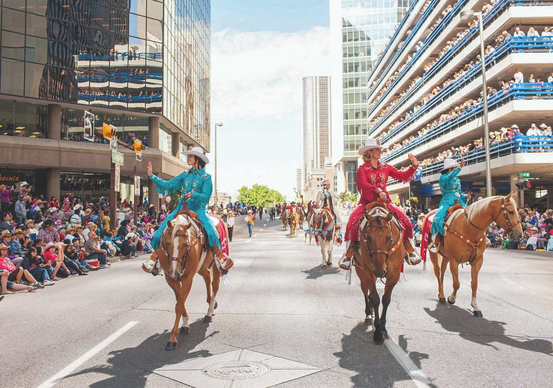 Un défilé avec des participants à cheval, des spectateurs sur les trottoirs et de grands immeubles en arrière-plan.