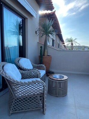 Ein Balkon mit Korbstühlen, einem runden Tisch und einem großen Blumentopf.
