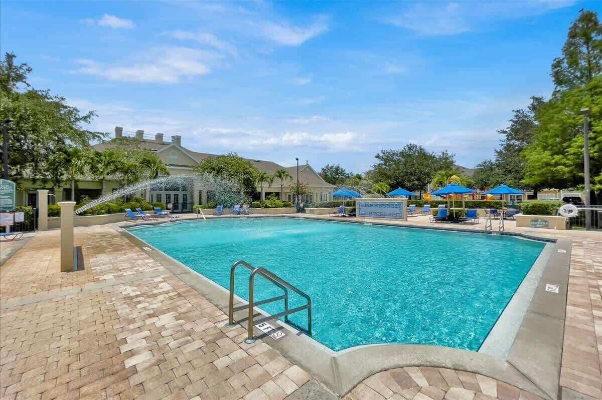 A rectangular swimming pool with a brick deck, a metal ladder, and blue umbrellas.