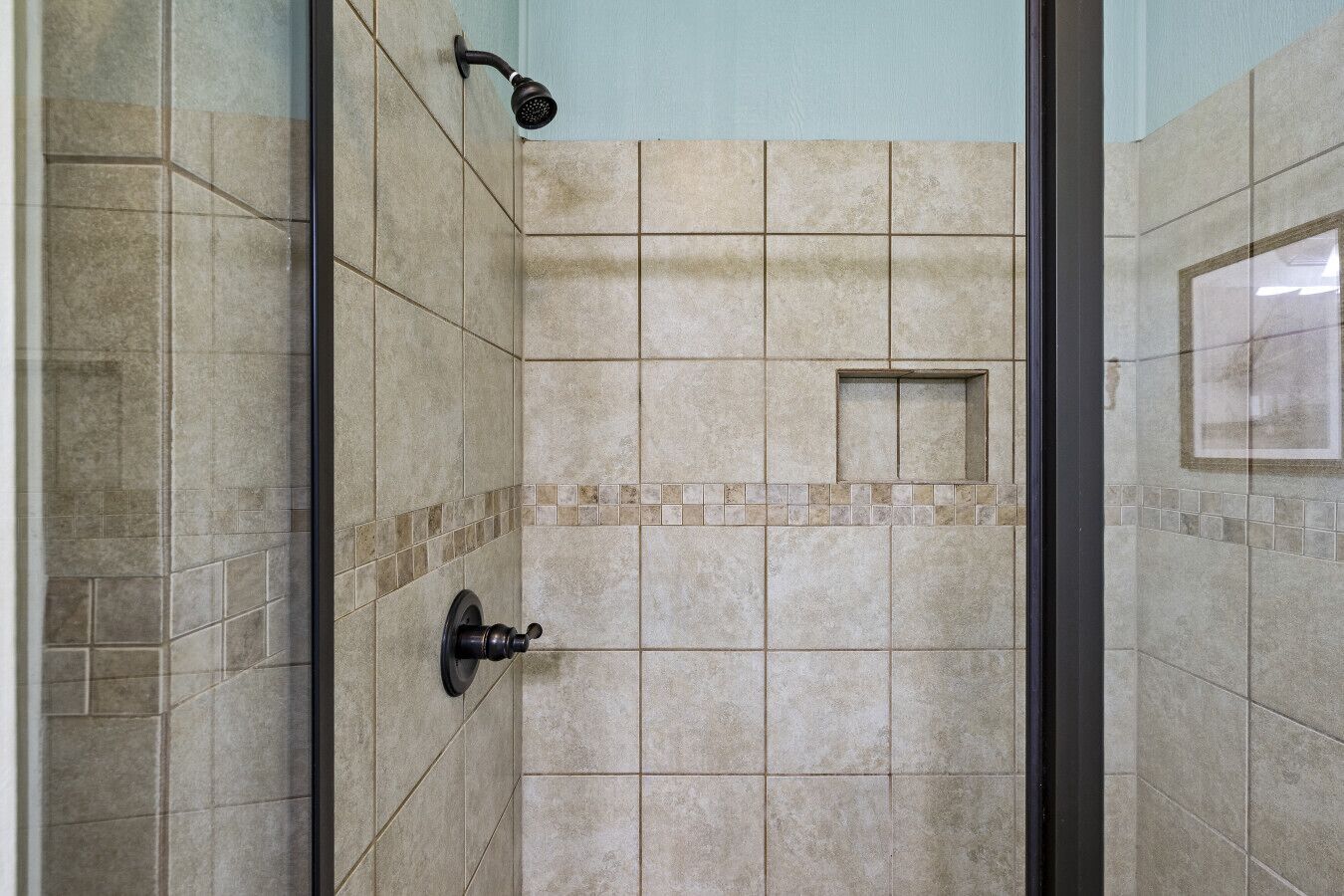 Een betegelde douche met een handdouche, een klein raam en een deur met een ronde knop.
