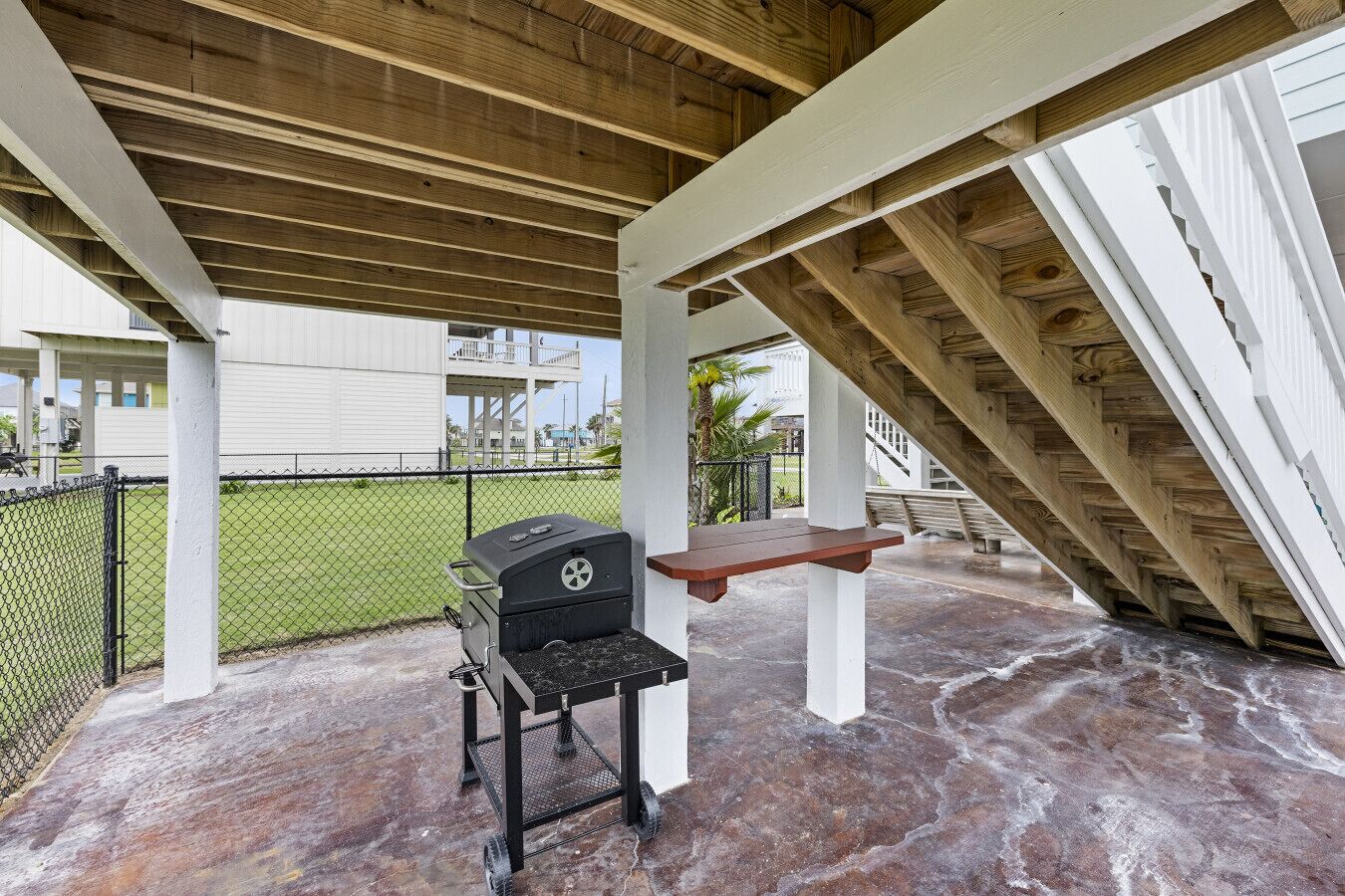 Un porxo cobert amb una barbacoa, una banca i vistes a una zona residencial.