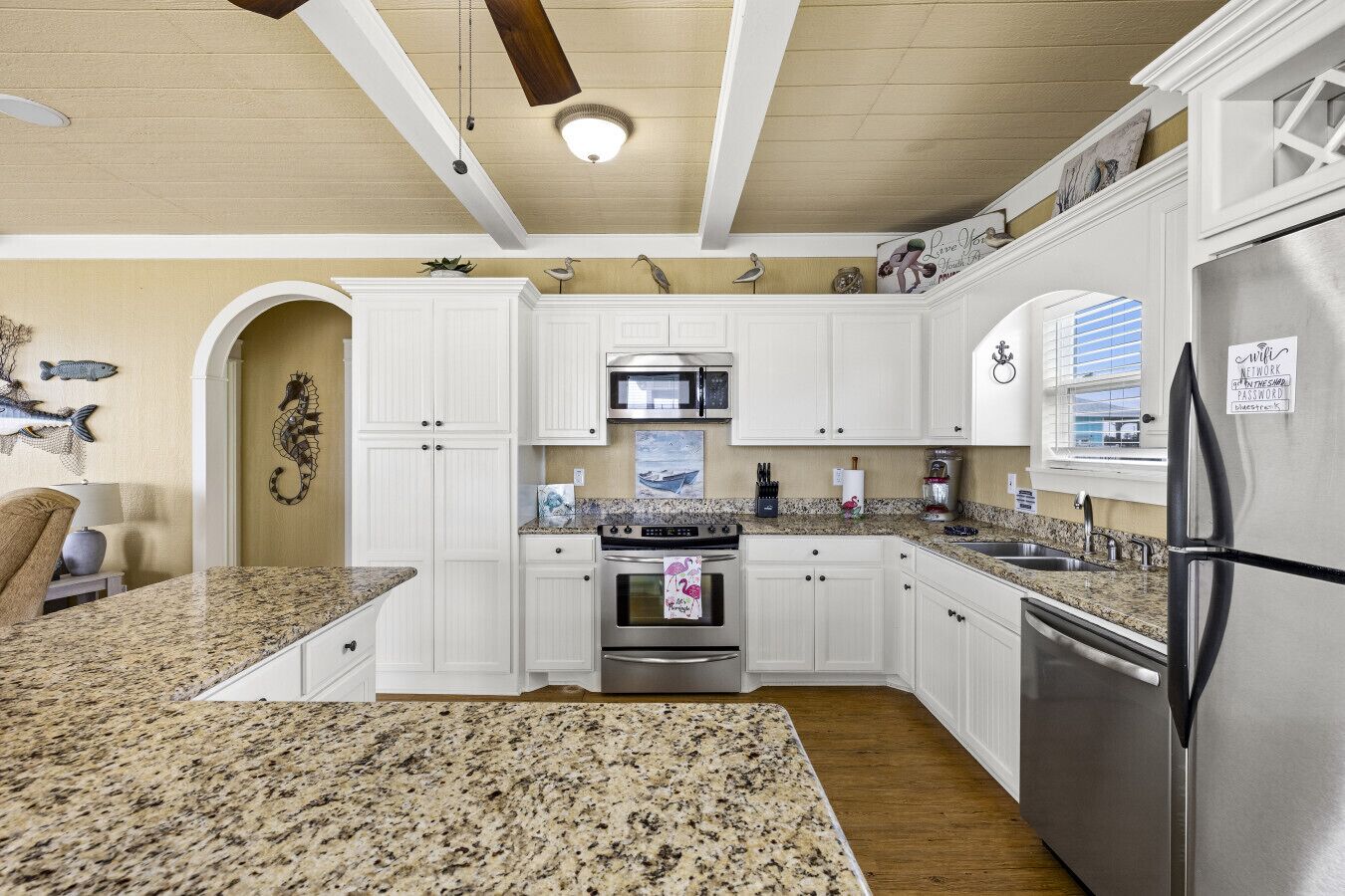 A kitchen with white cabinets, granite countertops, stainless steel appliances, and decorative wall art.