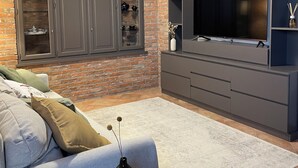 A living room with a brick wall, grey cabinets, a flat-screen TV, a sofa, and a coffee table with a candle.