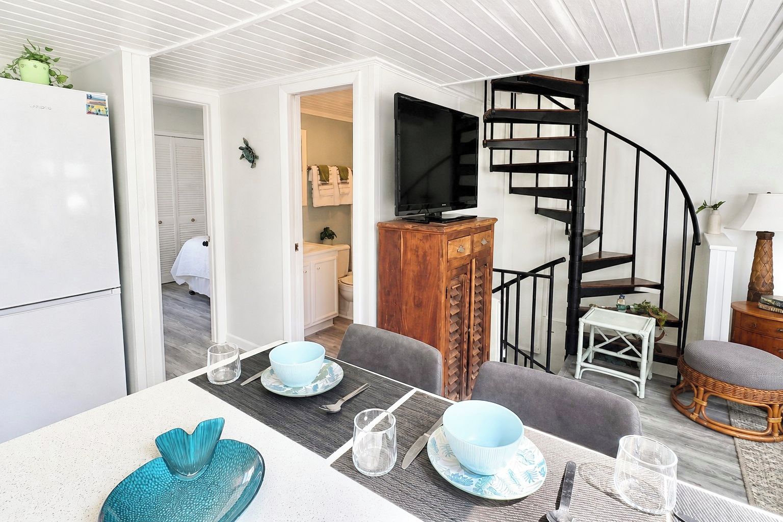 A compact living space with a dining area, a kitchenette, a television, and a spiral staircase.