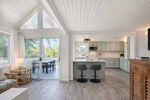 Una cocina amplia con una isla grande, puertas de vidrio corredizas que dan a un espacio exterior, y un comedor con mesa y sillas.