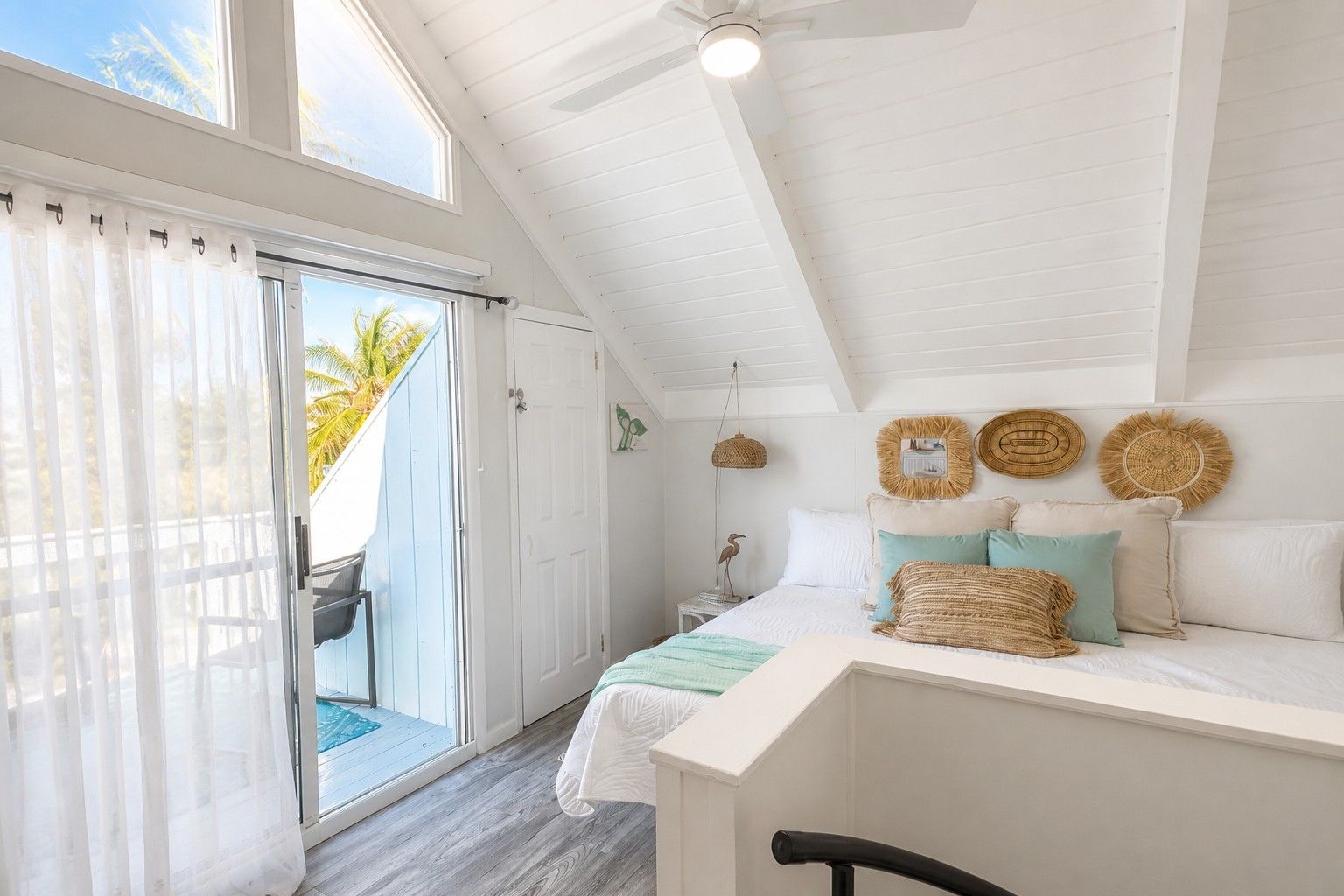 A bedroom with a bed, a ceiling fan, and a view of the outdoors.