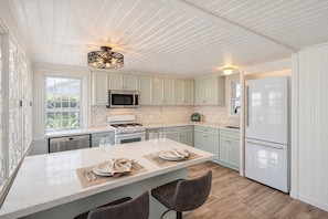 Una cocina moderna con armarios blancos, una isla central con asientos, microondas, estufa y refrigerador.