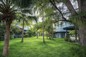 A well-maintained courtyard with palm trees, a building with a balcony, and a clear sky.