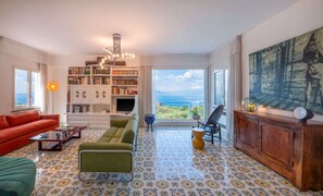 Un salon comprenant un canapé, des fauteuils, une bibliothèque, un téléviseur et un balcon avec vue.