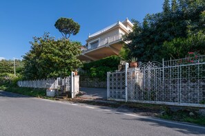 Un immeuble résidentiel doté d’un balcon, entouré d’une clôture blanche et de verdure.
